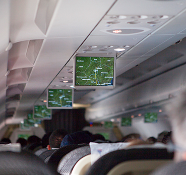 Imagem interna de avião com passageiros observando as telas de informação