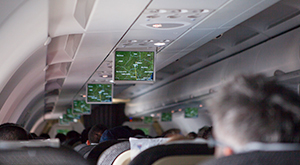 Imagem interna de avião com passageiros observando as telas de informação