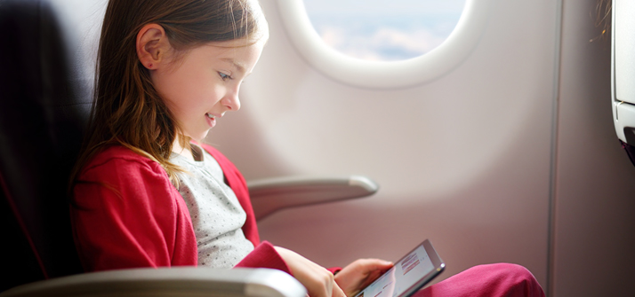 Criança sozinha na poltrona de um avião brincando com iPad.